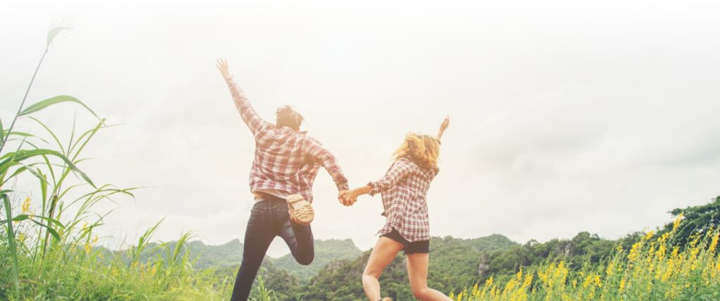 Two people joyfully leaping in a field, with a stripe of vibrant colors adding a dynamic touch.
