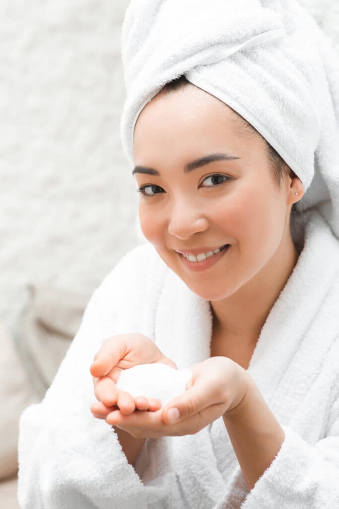 A woman in a bathrobe holding a soap bar, promoting the benefits of halotherapy with iVee Restorative Care.