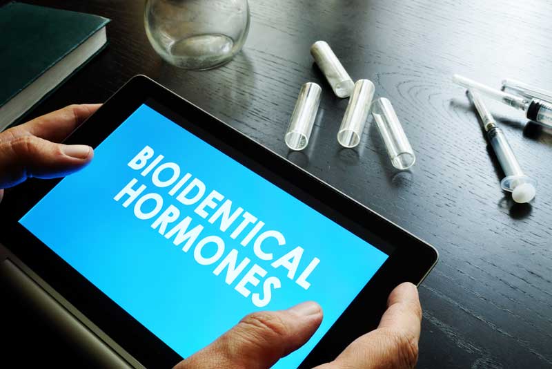 tablet written Bioidentical Hormones in blue background with a syringe in a table