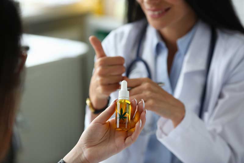 A female doctor holding a bottle of oil and giving a thumbs up gesture.