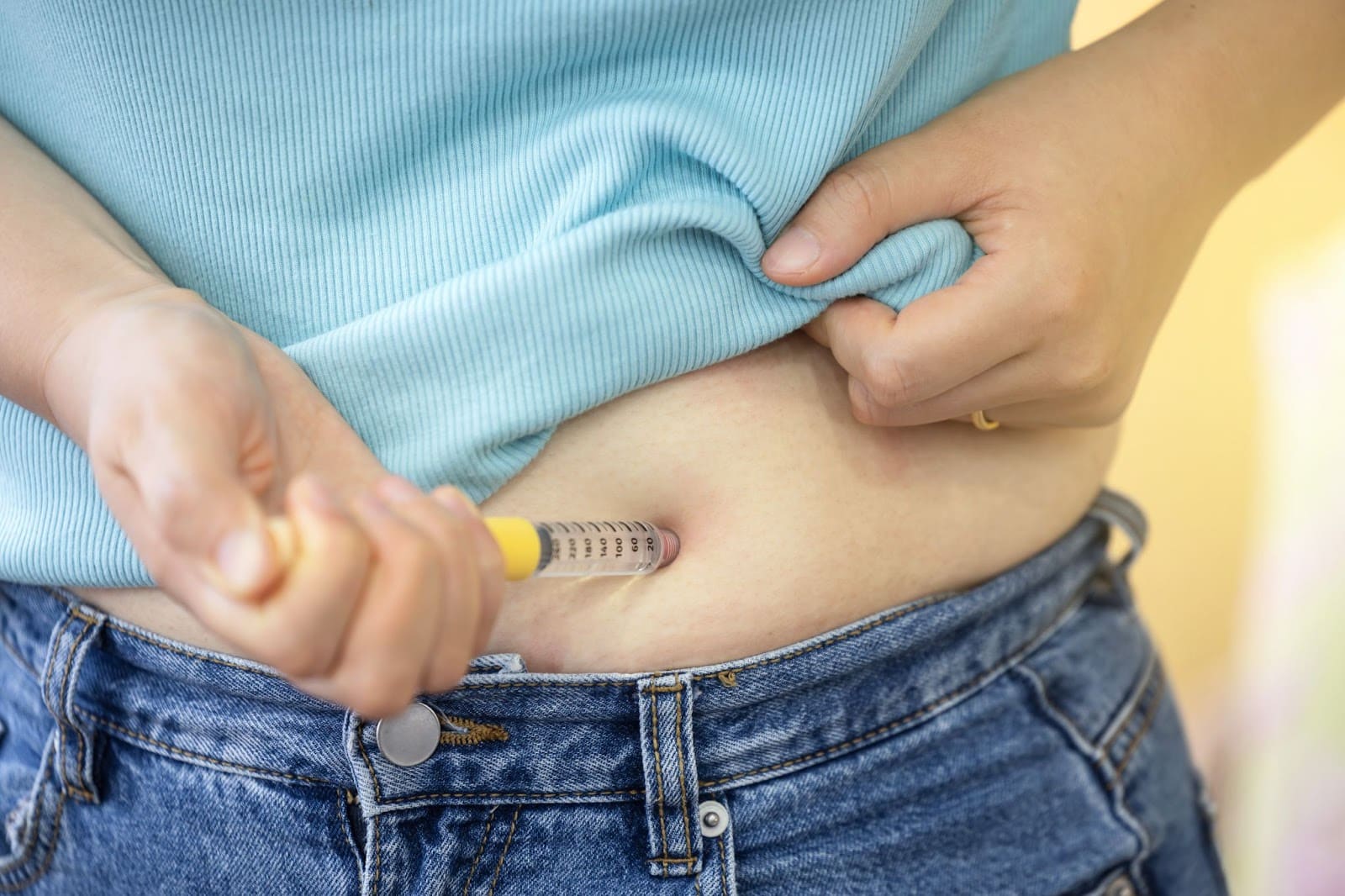 A woman holds a syringe to her stomach, symbolizing Semaglutide as a weight loss solution for effective weight management.